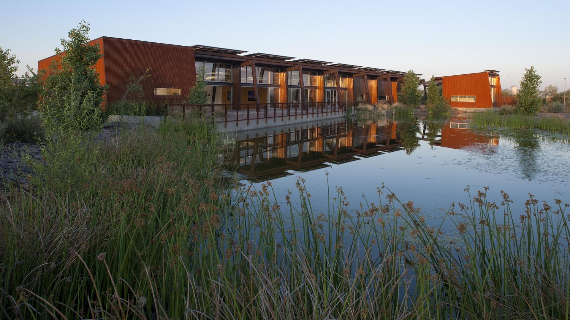 Water and tall grass in foreground of one story building at dusk